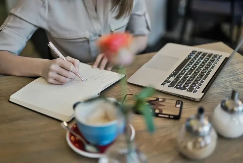 Person taking notes in front of a laptop in a casual environment