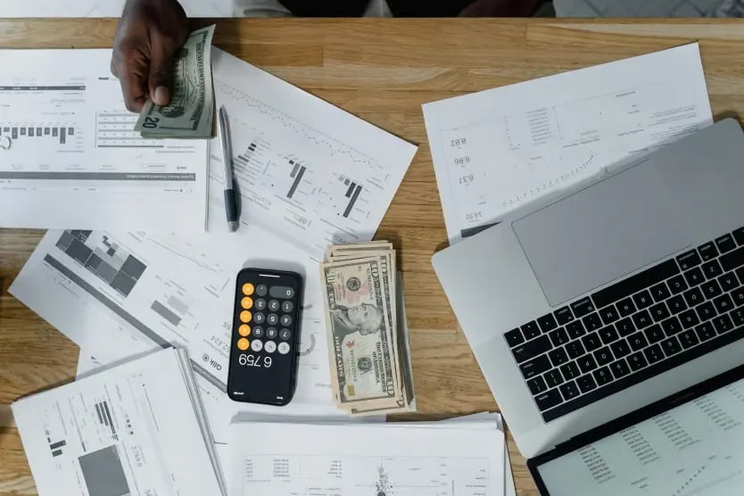 Person at a desk counting cash with accounting charts and devices nearby.
