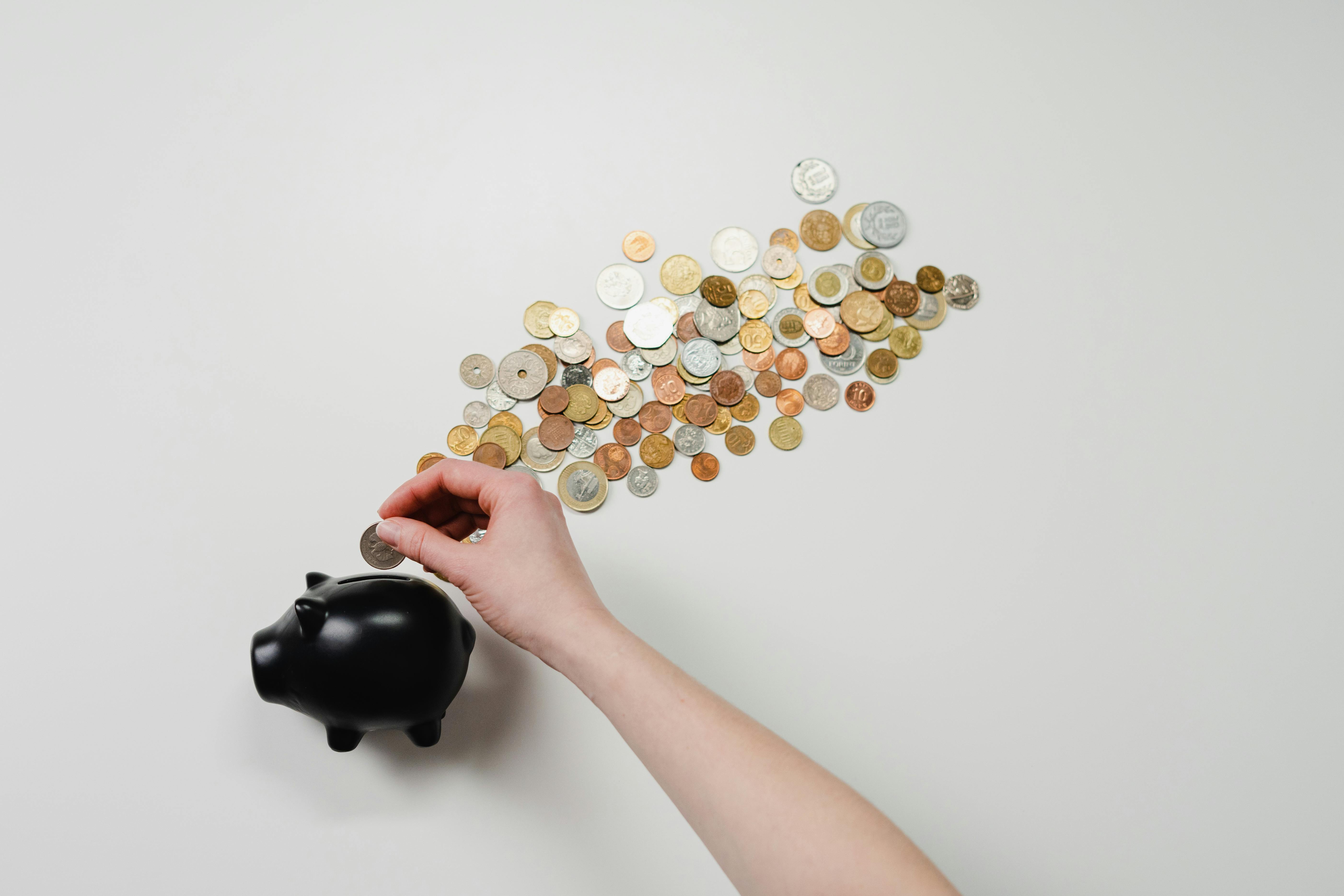 Person placing an assortment of coins into a small piggy bank.